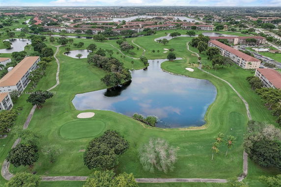 Aerial view of a landscape with buildings, lush greenery, trees, and a waterbody.
