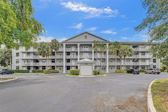 Front view of a multi-story residential building with balconies and palm trees.