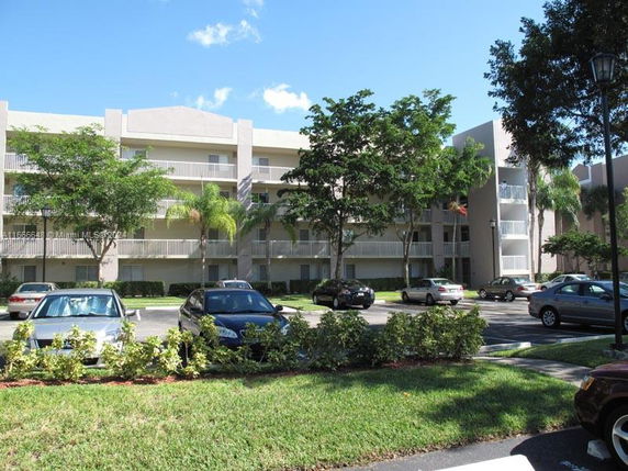 Front view of a multi-story apartment building with balconies and a parking area.