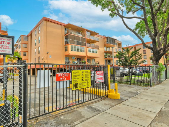 Front view of a multi-story apartment building with balconies and a gated entrance.