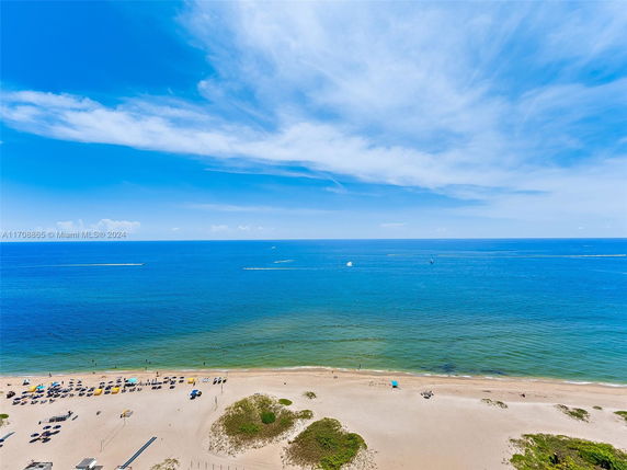 View of a sandy beach and ocean under a blue sky.
