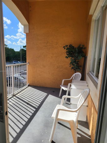 View from a balcony with two white chairs and a potted plant.