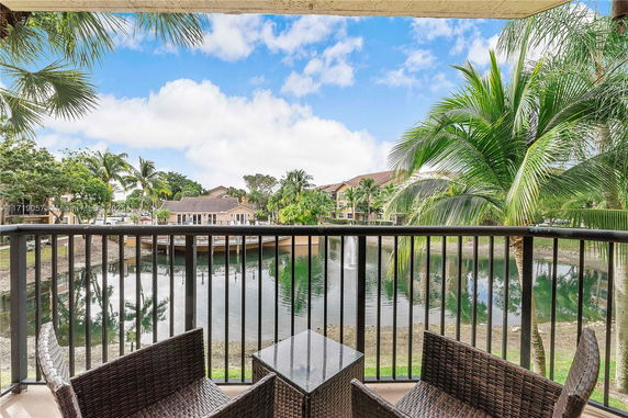 Balcony view of a pond with surrounding palm trees and residential buildings.