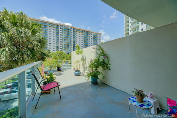 View from a balcony with potted plants overlooking a multi-story apartment building.