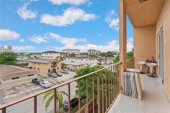 Balcony view of residential and commercial buildings in a neighborhood with parked cars and trees.