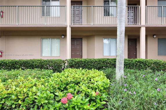 Front view of a multi-story building with balconies and shrubs in front.