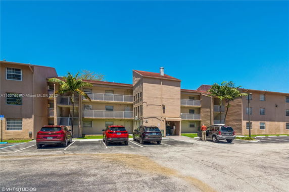 Front view of a multi-story apartment building with balconies and a parking area.
