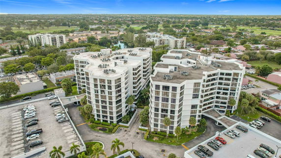 Aerial view of a complex of multi-story residential buildings with flat roofs and parking areas, set in a suburban landscape.