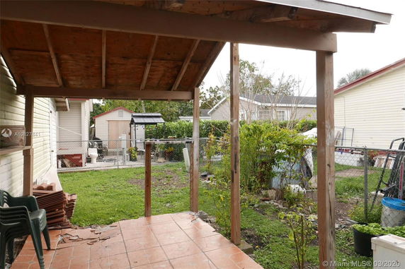 View of a backyard with a partially covered patio and several structures and plants.
