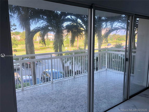 Balcony view from a building showing palm trees and a parking area.