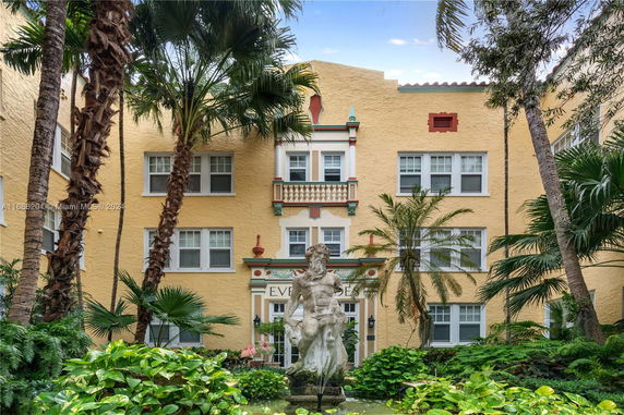 Front view of a yellow multi-story building with decorative architectural elements and a central statue fountain.
