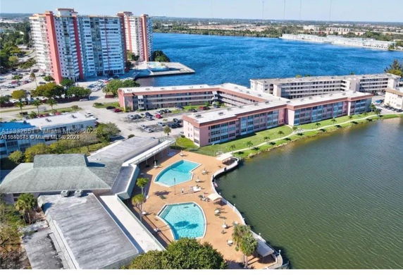 Aerial view of residential buildings near a body of water, with a swimming pool and surrounding facilities.