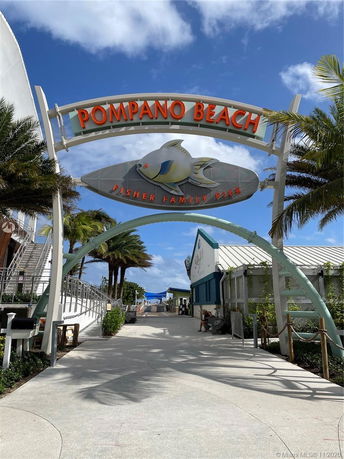 Entrance to Pompano Beach with an archway sign and walkway lined with palm trees.