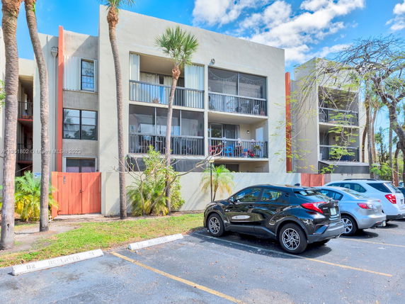 Front view of a multi-story apartment building with balconies and parking spaces.