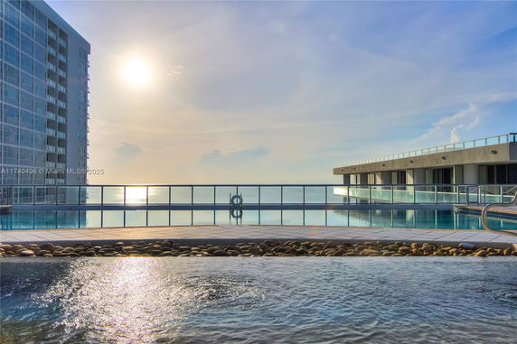 Outdoor swimming pool area with a view of modern buildings and the ocean in the background.