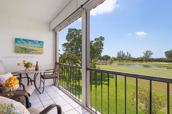 Balcony with a table and chairs overlooking a green landscape with trees and a small body of water.