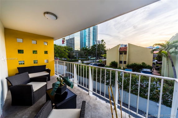 View from a balcony with outdoor seating overlooking buildings and a street.