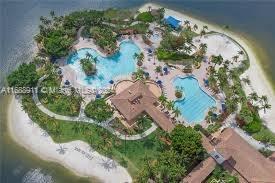 Aerial view of a large, resort-style swimming pool complex surrounded by sandy areas and lush greenery on an island.