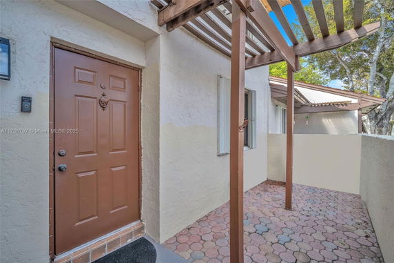 Exterior view of a house entrance with brown door and overhead pergola.