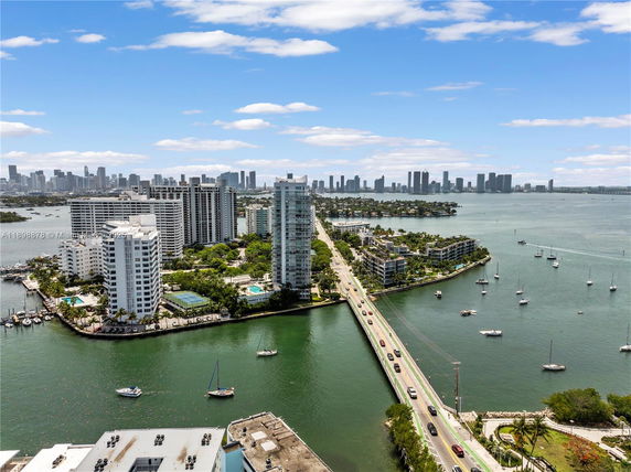 Aerial view of a waterfront cityscape with tall buildings, a bridge, and boats in the water.
