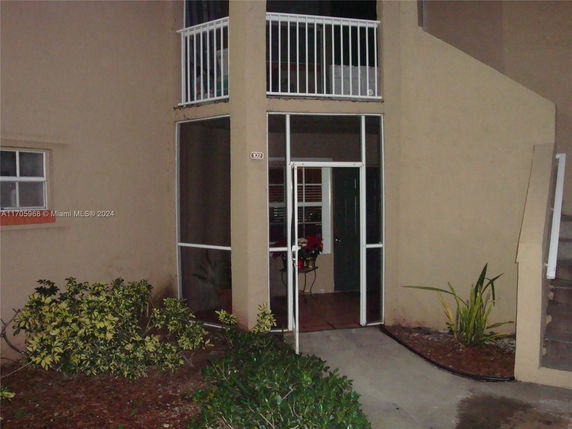 Front view of a building entrance with a screened door and balcony.