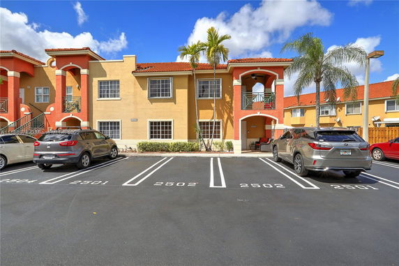 Outdoor parking spaces in front of a two-story apartment building with balconies.