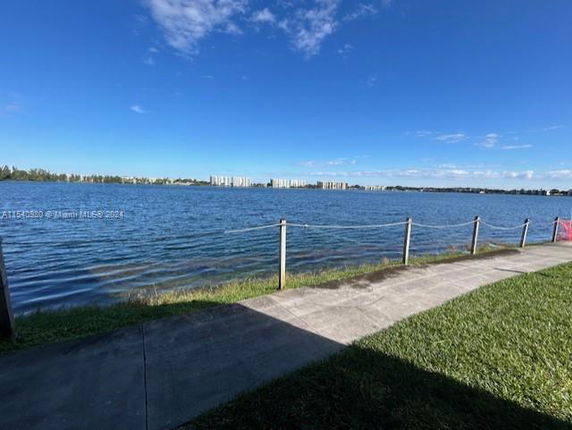 View of a large body of water with distant buildings and a railing along a pathway.
