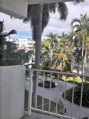 View from a building balcony overlooking a landscaped area with palm trees and a pathway.