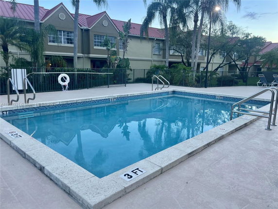 Outdoor swimming pool with surrounding poolside area and adjacent building with red roof.