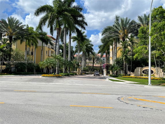Front view of a multi-story residential complex with palm trees and a gated entrance.