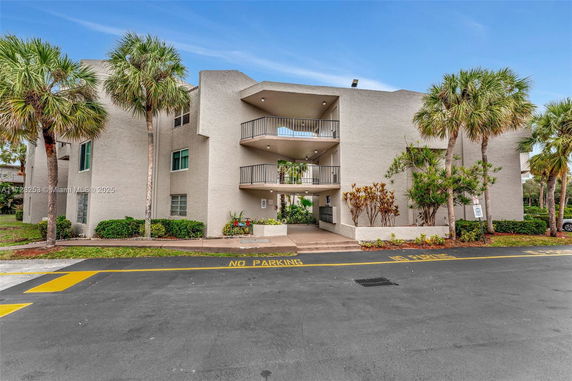 Front view of a multi-story building with balconies and a landscaped entryway.