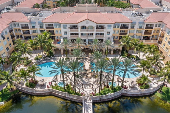Aerial view of a multi-story residential building with a swimming pool and palm trees in the foreground.