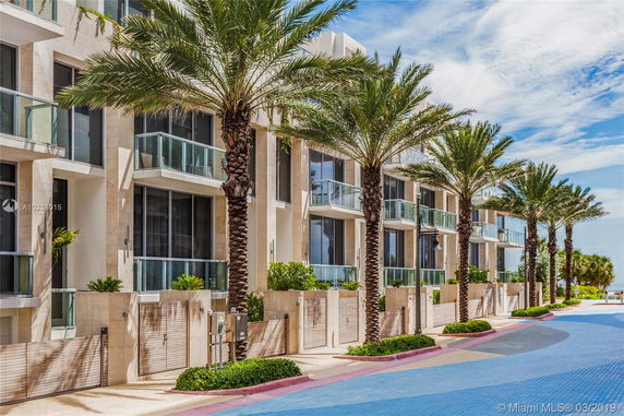 Front view of a modern multi-story residential building with balconies and palm trees.