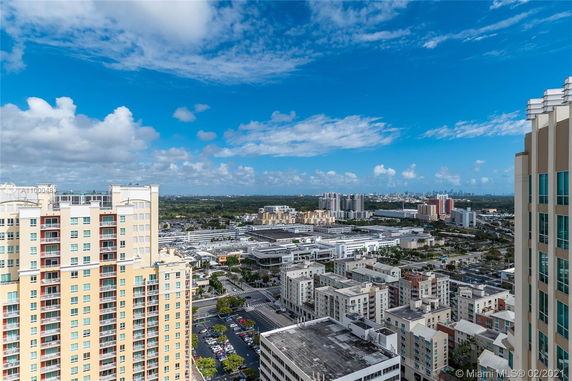 Panoramic view of city buildings and distant landscape under a blue sky with clouds.