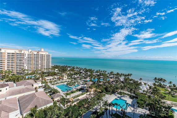 Panoramic view of a resort complex by the ocean with multiple swimming pools and palm trees, adjacent to a tall building.