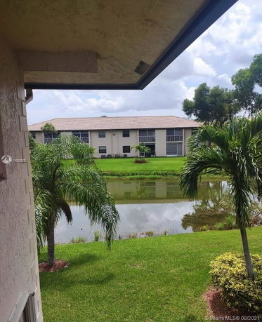 View of a multi-story building with a pond and palm trees in the foreground.