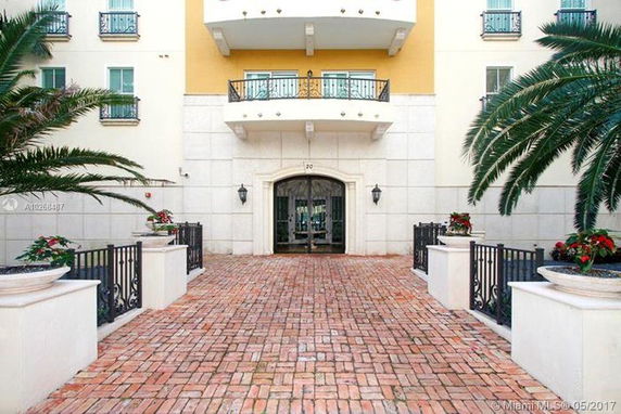 Front view of a multi-story building with balconies and a brick walkway leading to the entrance.