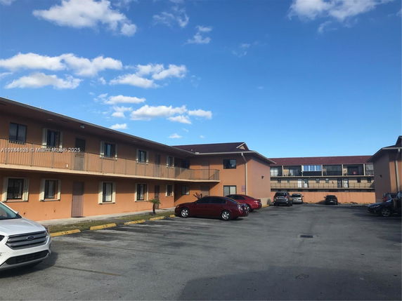 Outdoor parking area in front of a two-story building with multiple parked cars.