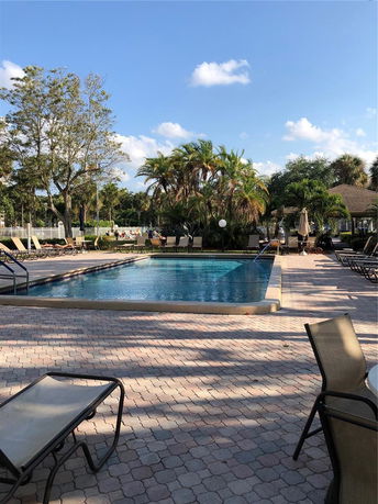 View of an outdoor swimming pool surrounded by lounge chairs and palm trees.