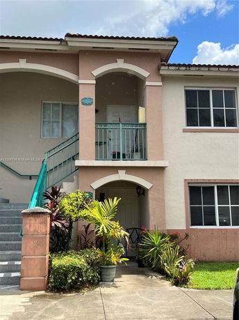Front view of a two-story building with a staircase leading to an upper entrance, featuring arches and a small garden.