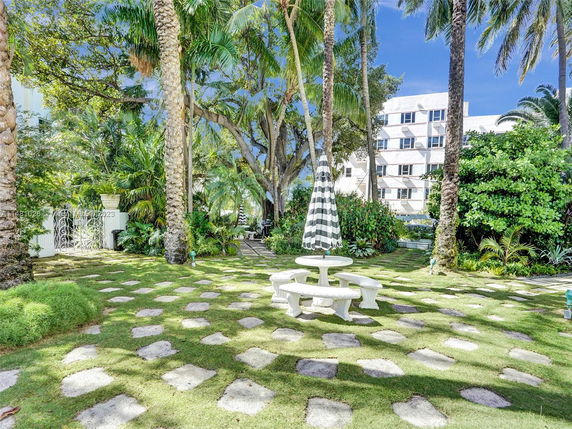 Outdoor area with palm trees, a stone path, and a white multi-story building in the background.