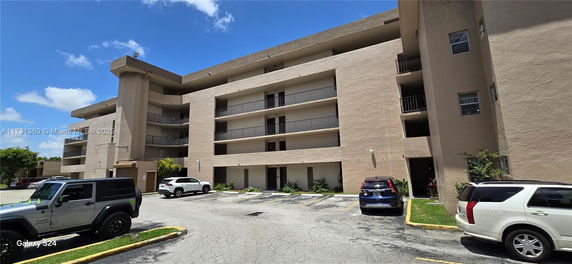 Front view of a multi-story residential building with visible balconies and parking area.