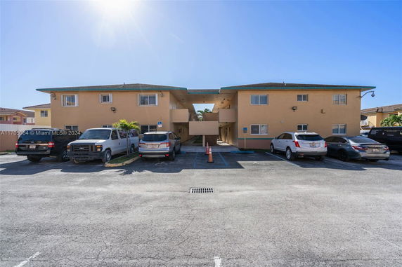 Front view of a two-story apartment building with multiple cars parked in front.