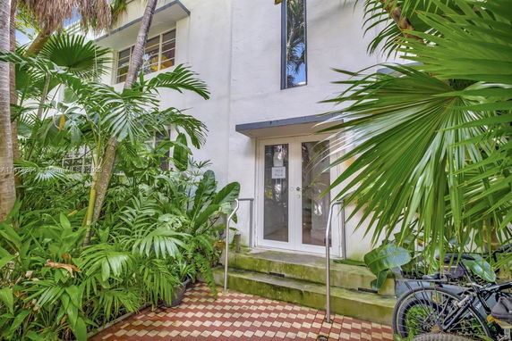 Front view of a house entrance with glass doors surrounded by tropical plants.