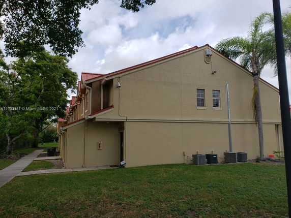 Side view of a beige two-story building with red roof accents and visible air conditioning units.