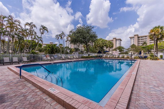 Outdoor swimming pool area with surrounding buildings and palm trees.