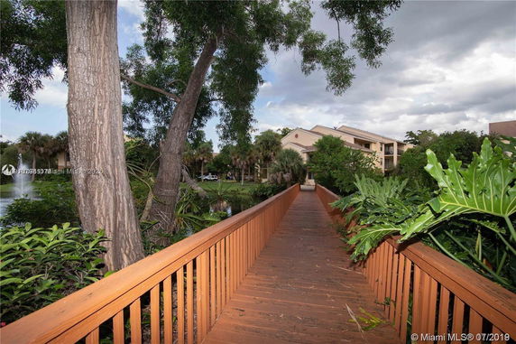 Front view of a multi-story building with a wooden walkway and lush greenery.