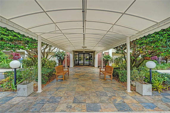 Entrance area with a covered walkway and seating, leading to building doors.
