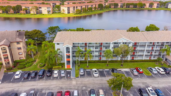 Aerial view of a multi-story residential building next to a parking lot and a lake.