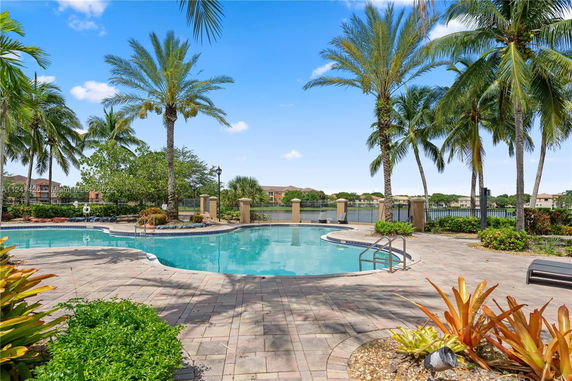 Outdoor swimming pool area with palm trees and interlocking stone deck.